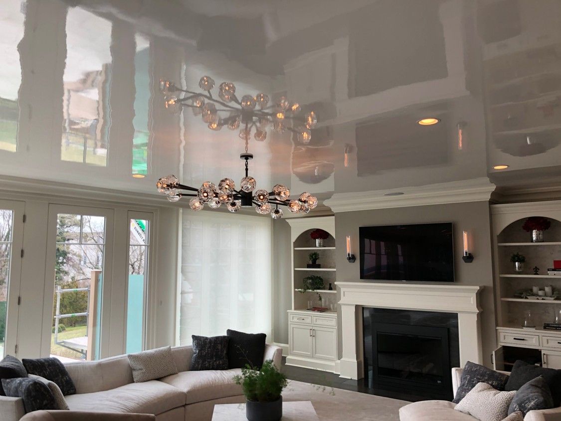 Bright living room with tall windows, a chandelier, fireplace, TV, and gray sofas