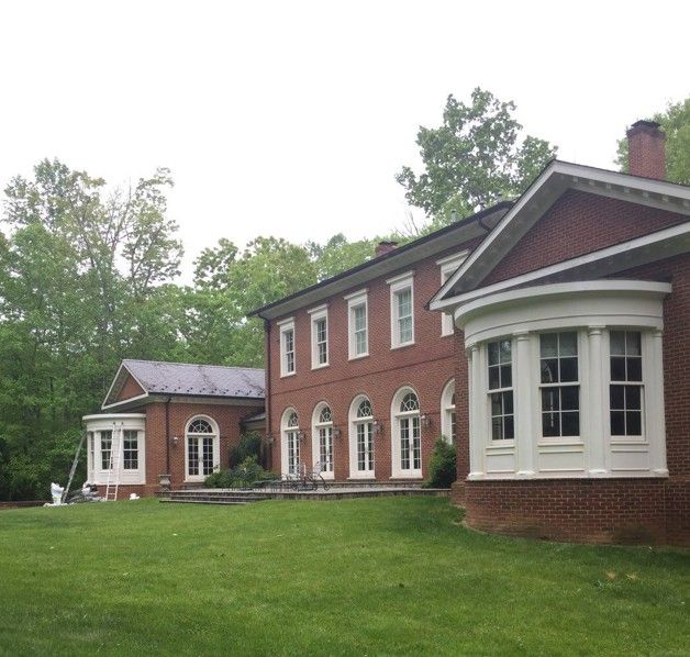 Large red-brick house with white-trimmed bay windows and a green lawn, surrounded by trees