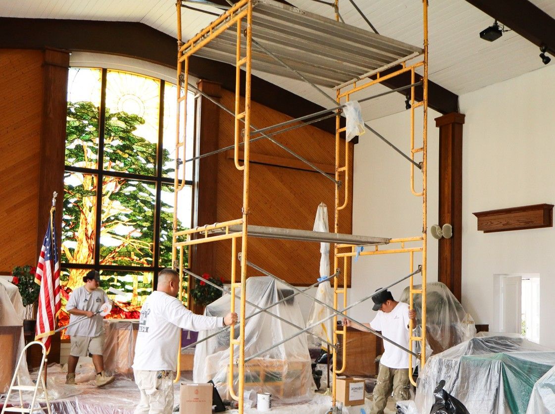 Workers on scaffolding painting a church interior with white walls and a wooden altar backdrop