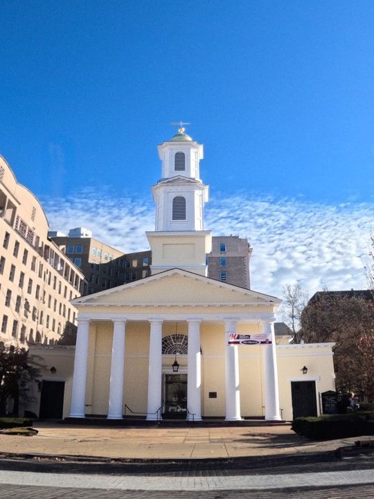 White church with tall steeple and columns on a sunny street under a blue sky.