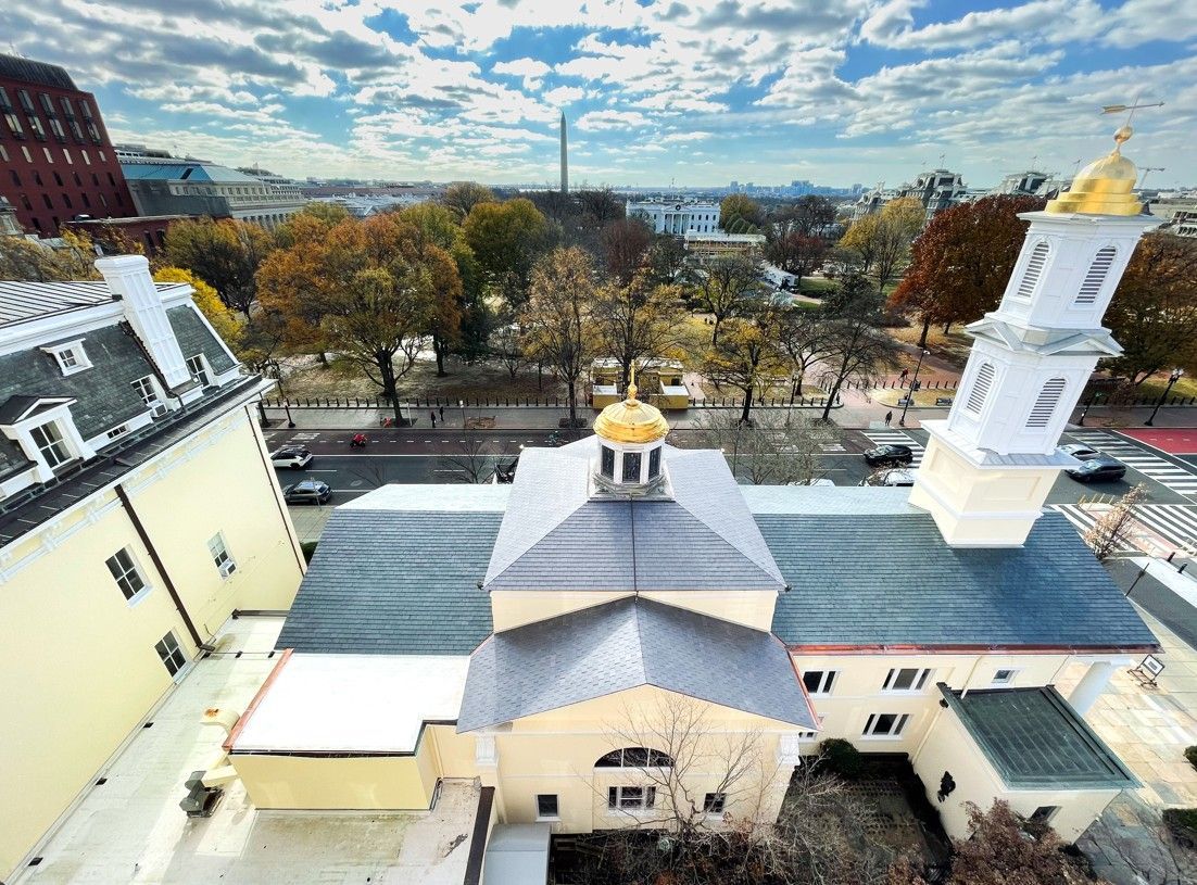 Aerial view of a white church with a gold dome, surrounded by autumn trees and city buildings