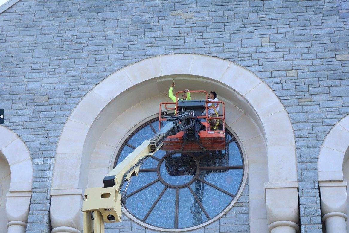 Worker in a lift repairing a circular window on a stone building facade