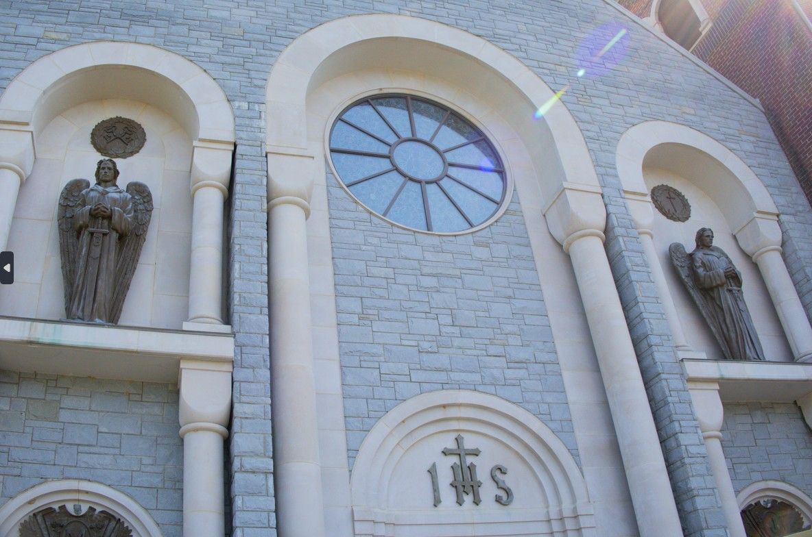 Stone church facade with arched niches, statues, and a circular stained-glass window