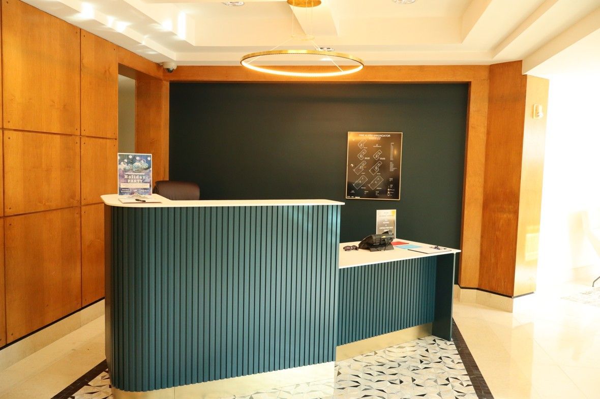 Hotel reception desk with teal front panel in a warmly lit lobby with wood-paneled walls.