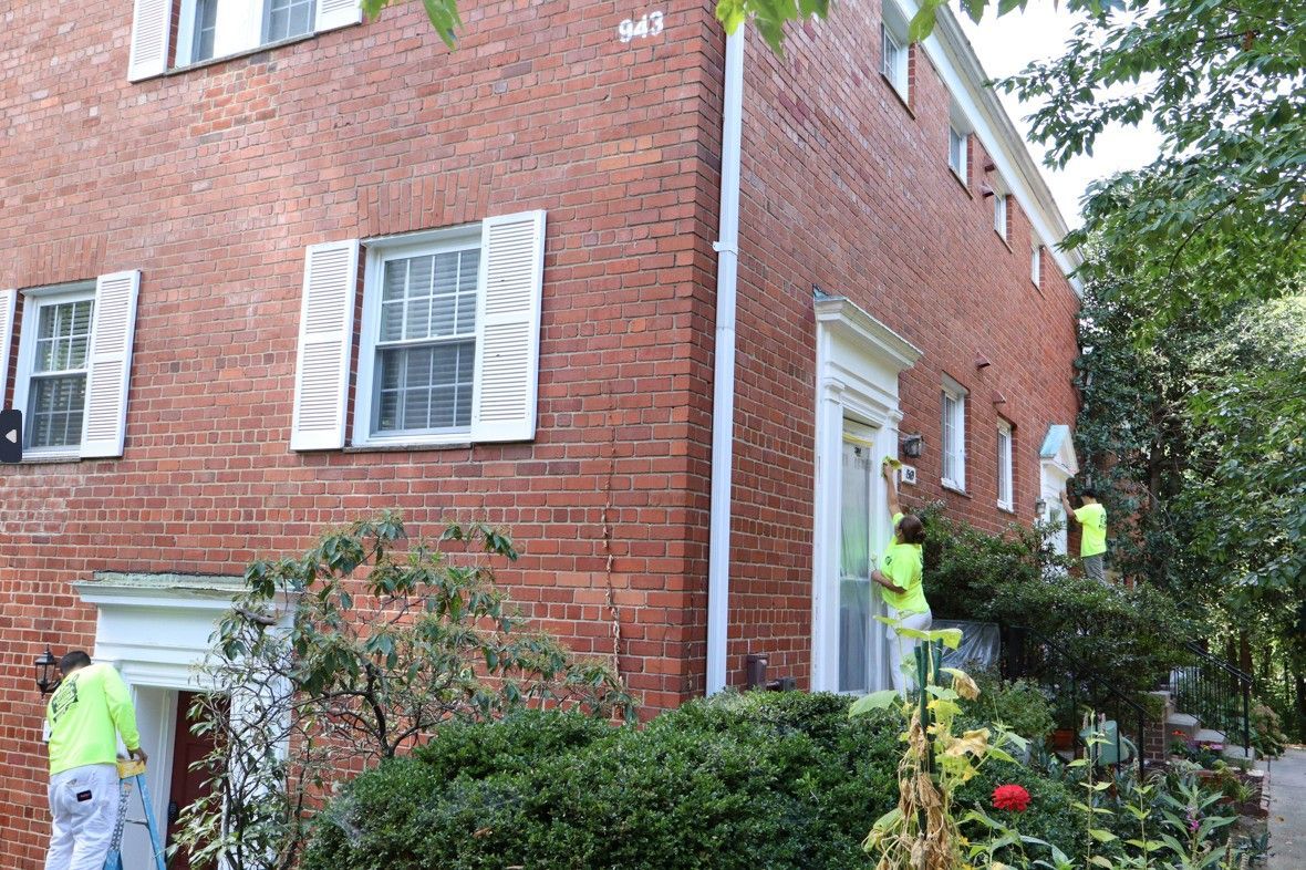 Workers in neon jackets inspecting a brick house exterior near a white door and shrubs