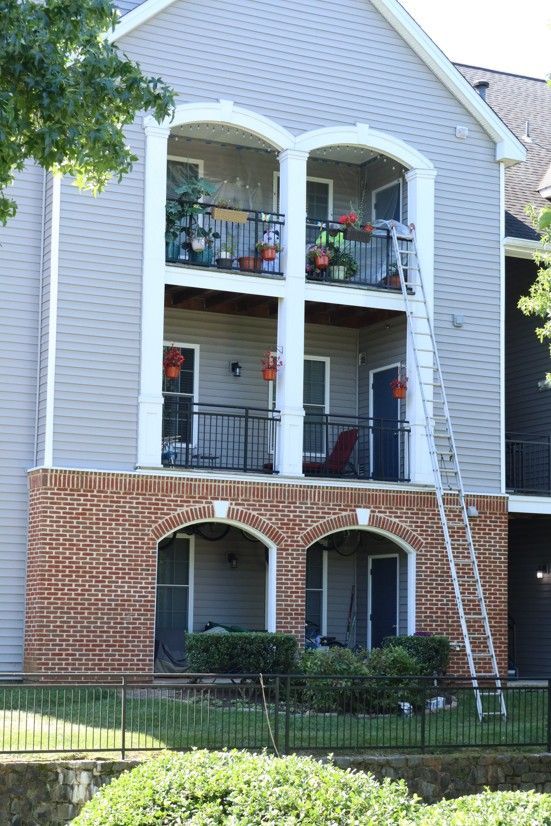Three-story apartment building with balconies, white siding, red brick, and a ladder leaning against it