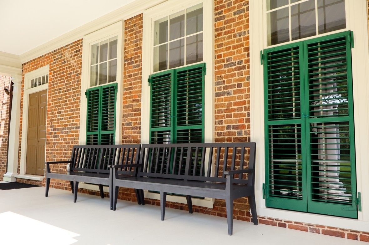 Brick porch with green shutters and dark wooden benches along the wall.