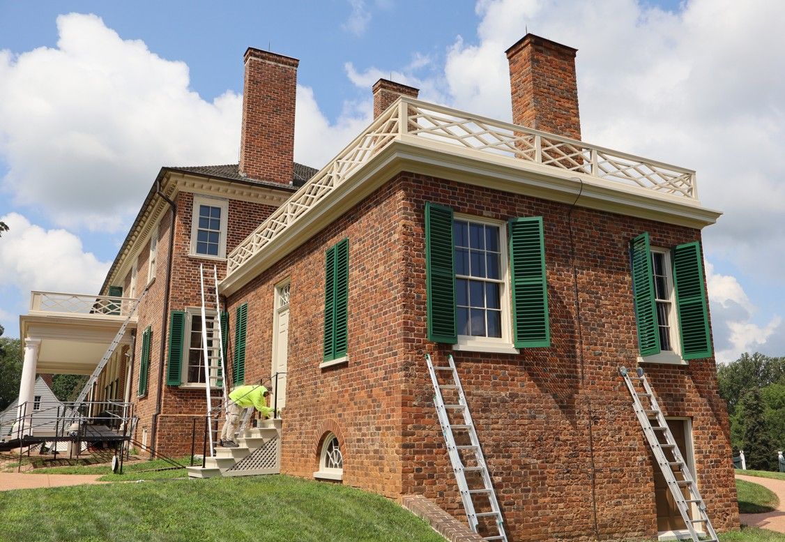 Historic red-brick house with green shutters and white trim on a grassy lawn
