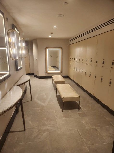 Empty locker room with benches, mirrors, sinks, and beige lockers under soft lighting