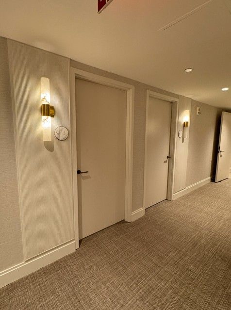 Quiet hotel hallway with closed white doors, wall sconces, and beige carpet.