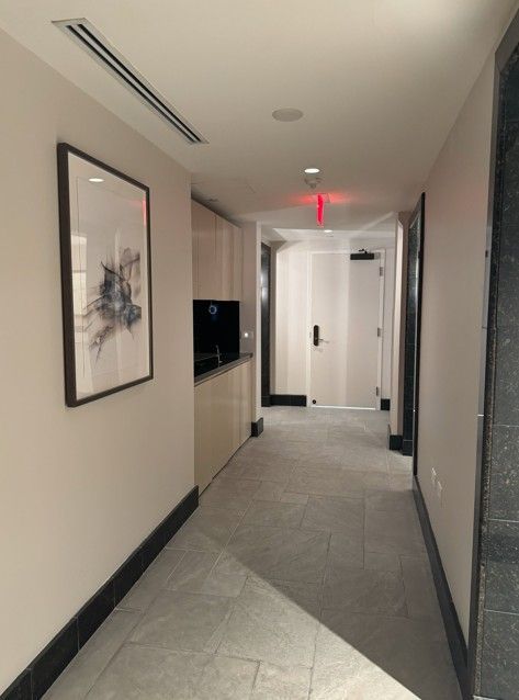 Narrow beige hallway with framed wall art, gray carpet, and white doors at the end