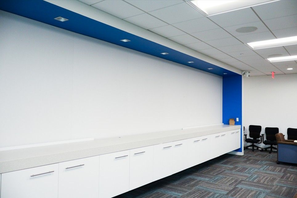 Modern office break area with white cabinets, blue accent wall, and black chairs on carpet