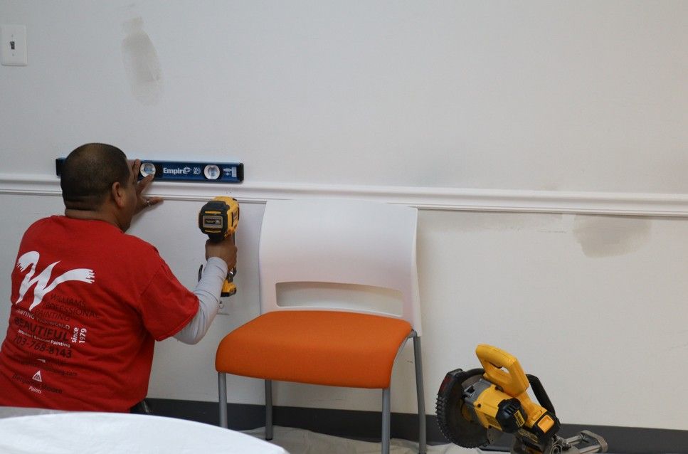 Person using a yellow drill to mount a white rail above an orange chair in a room with a white wall
