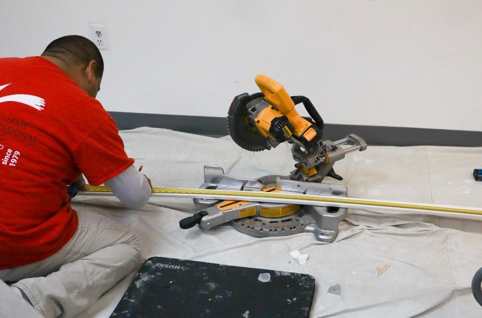 Worker in red shirt cutting tile with a miter saw on a floor covered in dust and tools