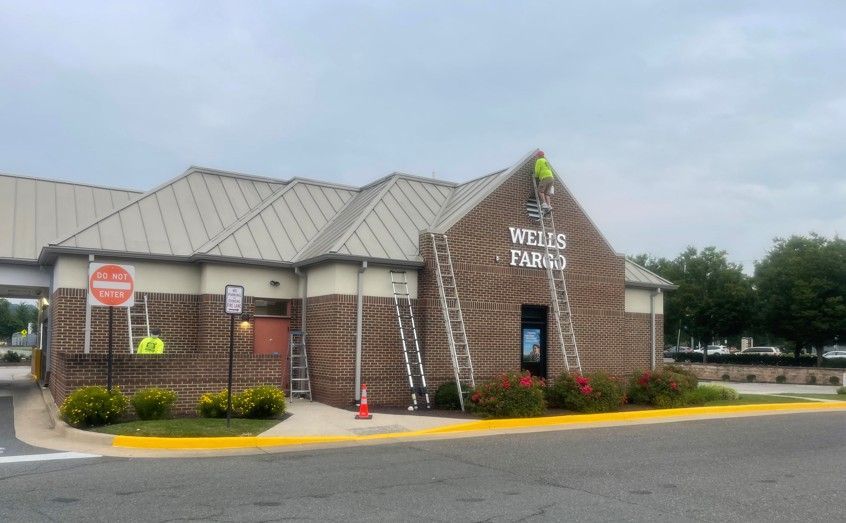 Brick drive-thru banking kiosk with a silver roof and wet pavement at dusk