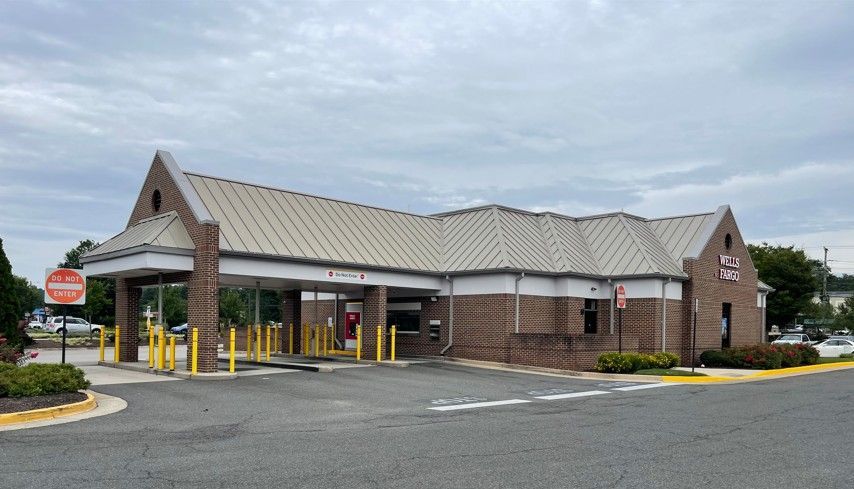 Brick bank branch with drive-thru lanes, yellow bollards, and a cloudy sky