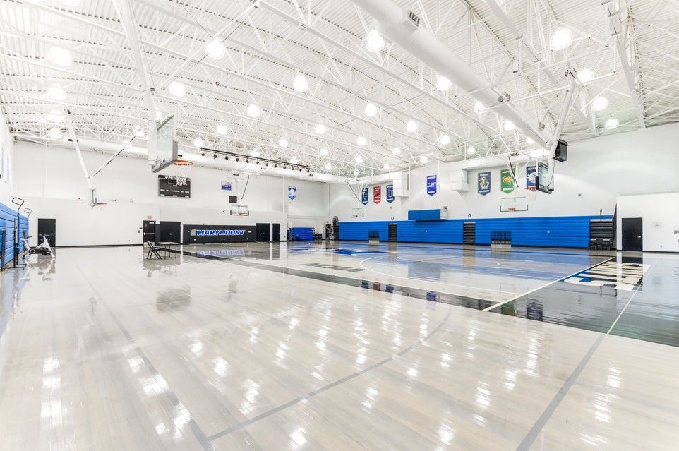 Empty indoor gym with polished floor, blue wall pads, and bright overhead lights