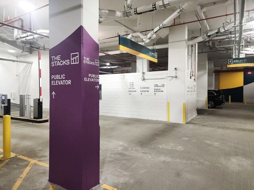 Parking garage with a purple pillar marked “PUBLIC ELEVATOR” and a white wall ahead.