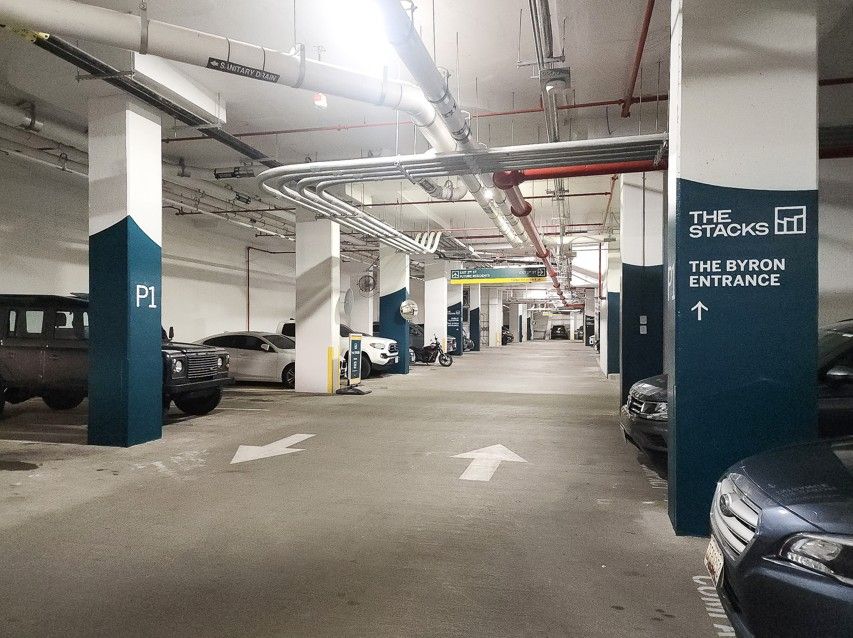 Underground parking garage with cars, white arrows, and blue-gray pillars under bright overhead pipes
