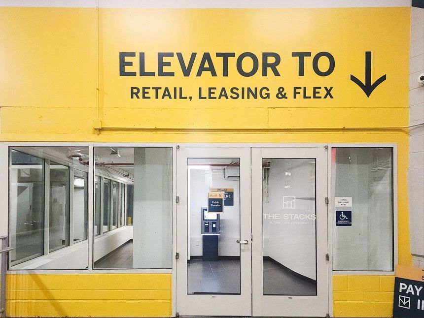Yellow elevator entrance with sign reading “ELEVATOR TO RETAIL, LEASING & FLEX” above glass doors.