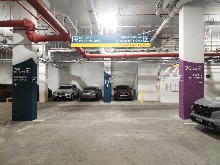 Underground parking garage with parked cars, concrete pillars, and overhead pipes and signs.