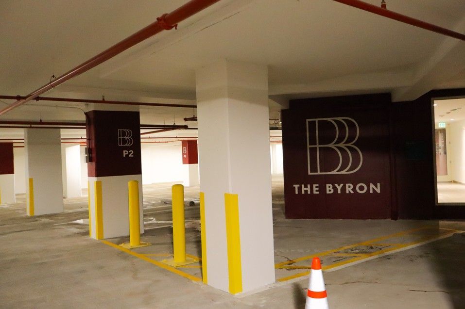 Parking garage with yellow bollards and a black wall sign reading “The Byron”