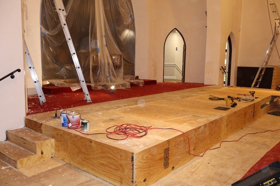Wooden platform under construction in a room, with tools, cords, and ladders around it.