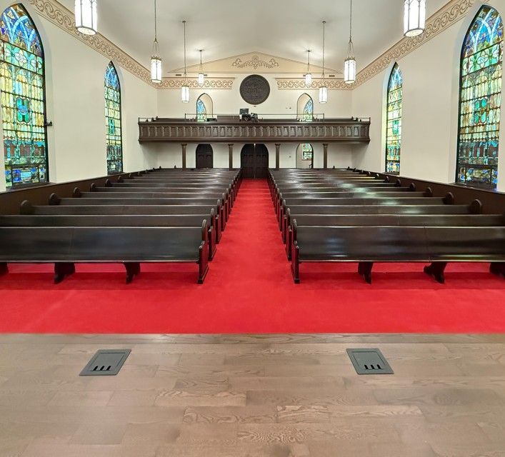 Empty church sanctuary with red carpet aisle, dark pews, stained-glass windows, and balcony altar area