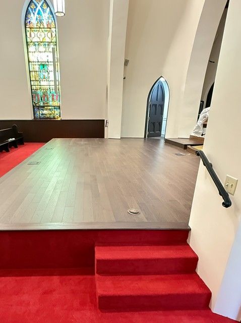 Church sanctuary with red-carpeted steps leading to a raised wooden platform and stained-glass window.