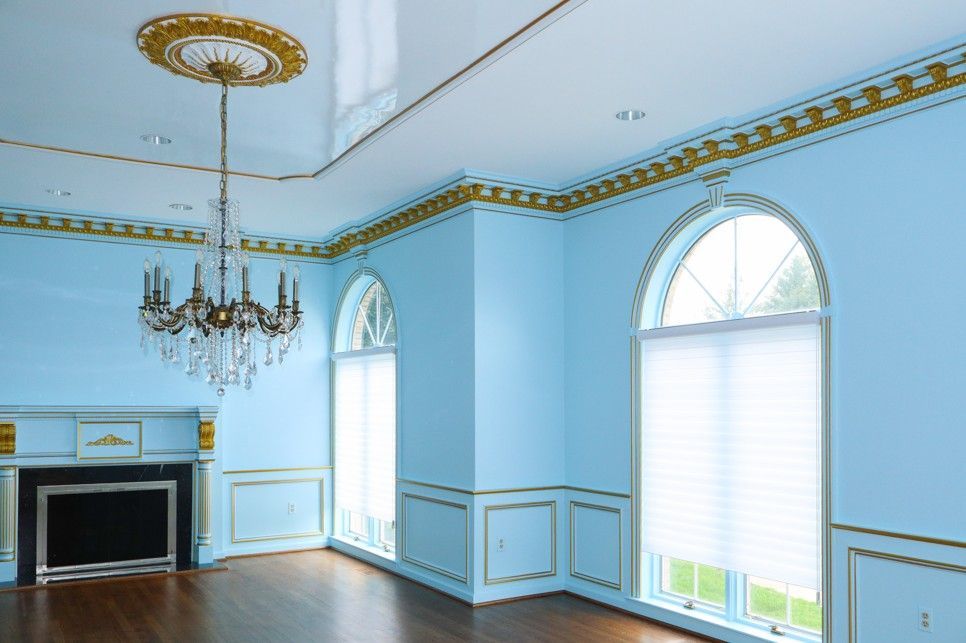 Elegant light-blue room with fireplace, chandelier, and arched windows with blinds