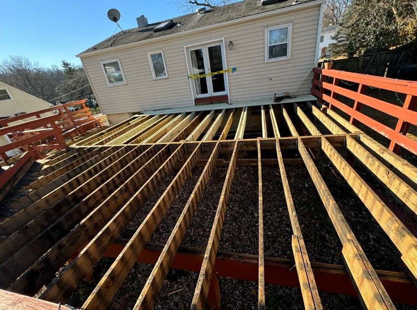 Back deck under construction beside a beige house, with exposed joists and red railings.