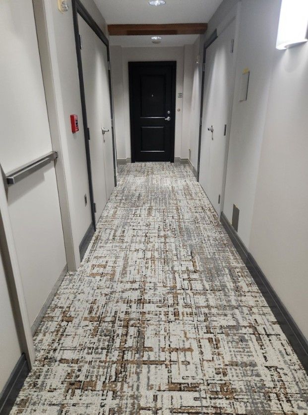 Empty hallway with patterned carpet, white walls, and a dark door at the end.