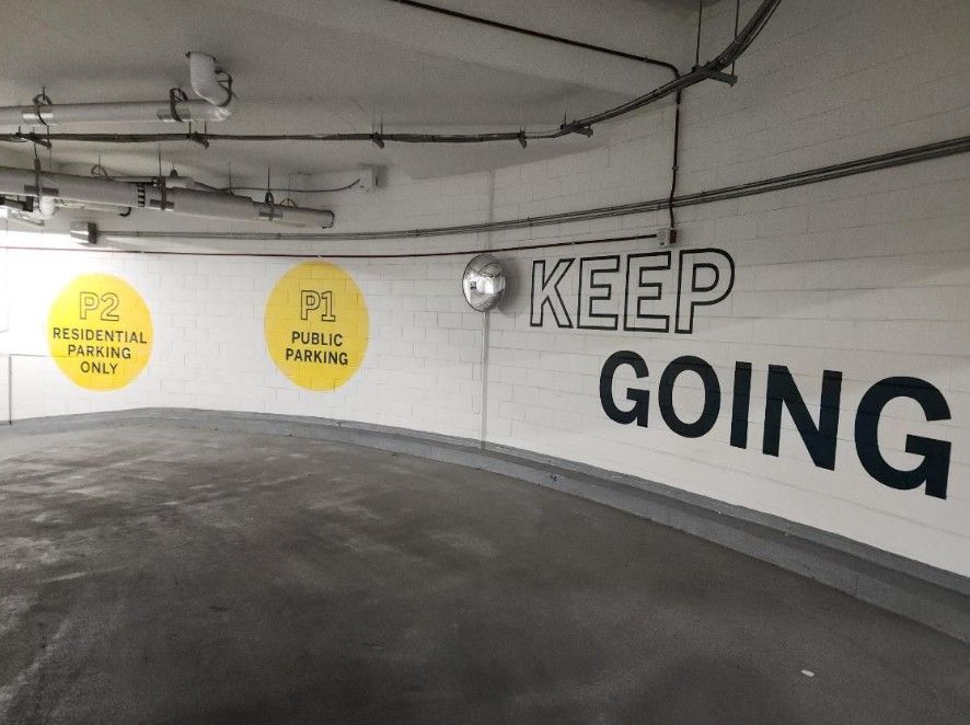 Parking garage wall with yellow signs and large black “KEEP GOING” text