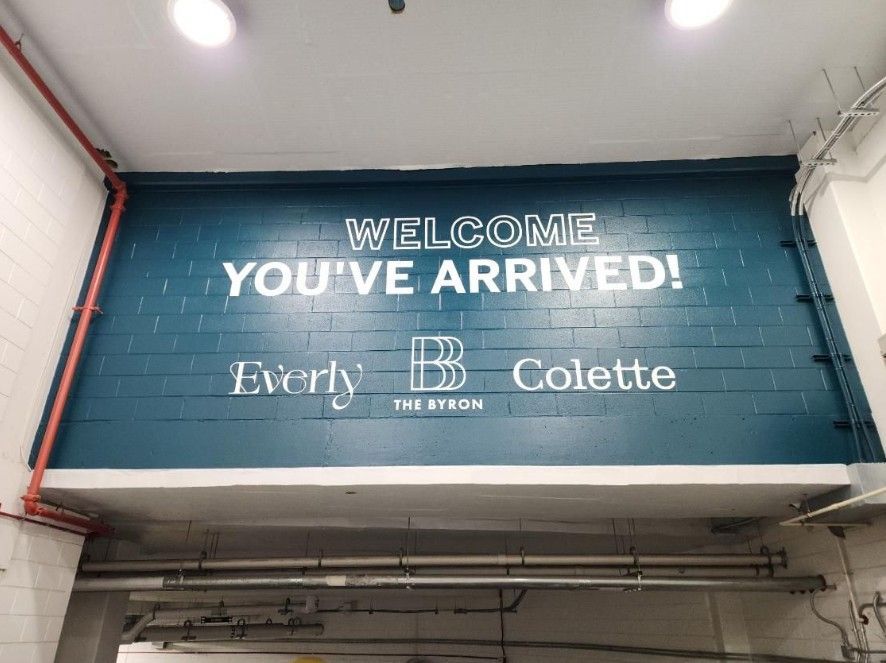 Blue wall sign reading “WELCOME YOU’VE ARRIVED!” with Everly and Colette logo underneath