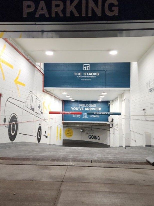 Parking garage entrance with blue service signs, white walls, and a car mural on the left.