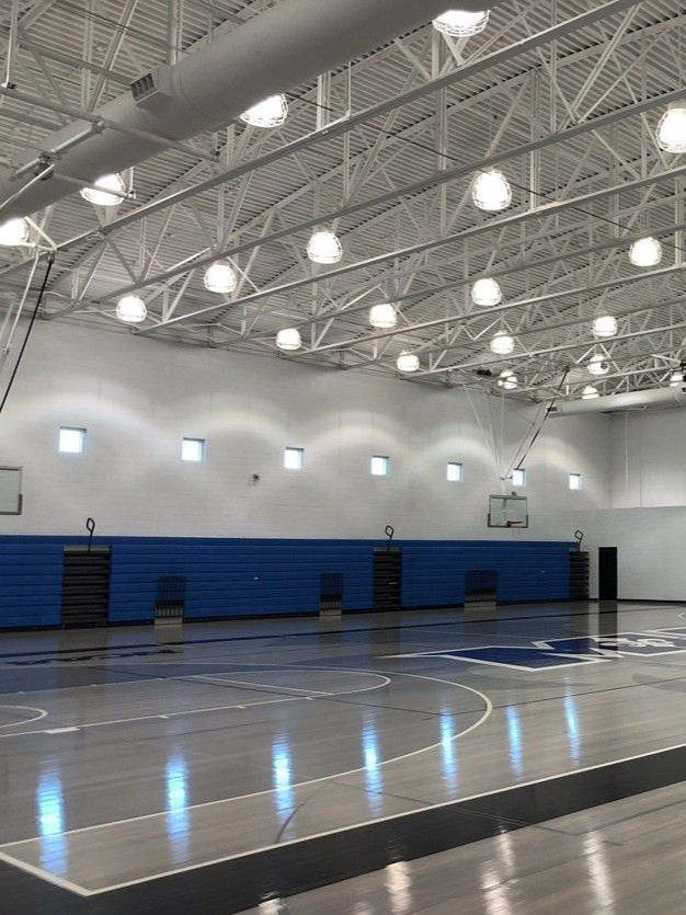 Empty indoor basketball gym with blue bleachers and bright ceiling lights