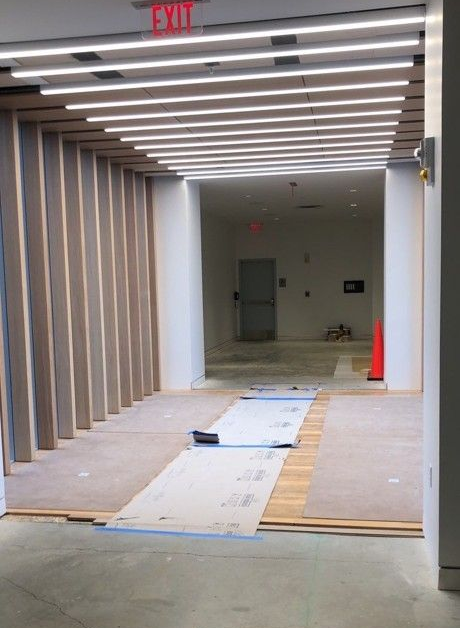 Renovated hallway under construction with exposed framing, ceiling lights, and floor protection mats leading to a doorway