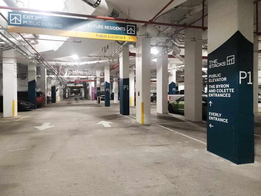 Empty indoor parking garage with concrete pillars, overhead signs, and parked cars.