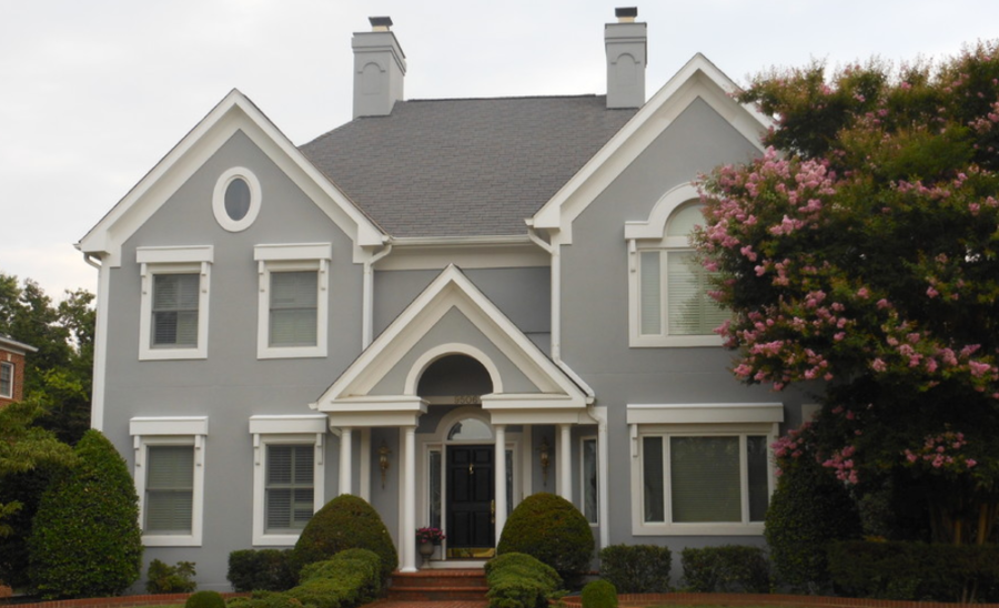 Gray two-story house with white trim, arched entryway, and flowering tree in front