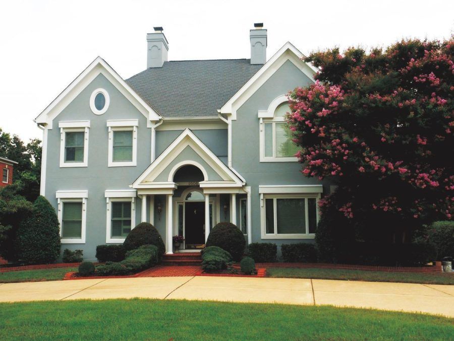 Two-story gray house with white trim, arched front porch, and large pink-flowering tree on the right