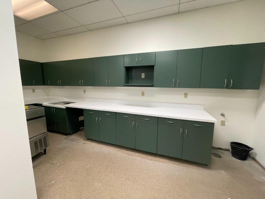 Empty break room with dark green cabinets, white countertops, and beige tiled floor
