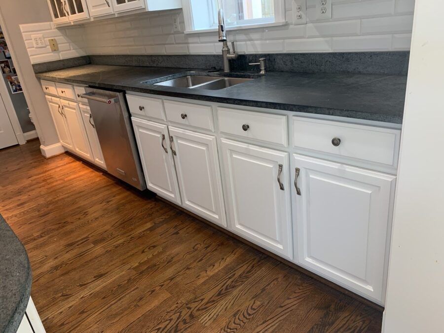 White kitchen with dark countertops, stainless dishwasher, sink, and wood-pattern floor.