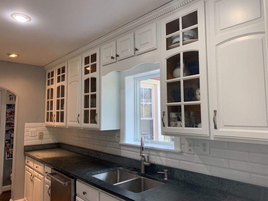 Bright white kitchen with black countertops, glass-front cabinets, sink, and tiled backsplash