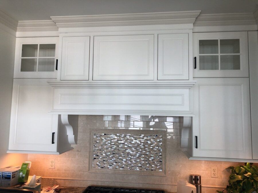 White kitchen cabinets above a stove with a decorative tile backsplash and under-cabinet lighting