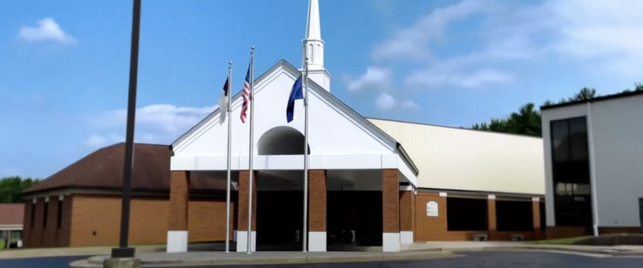 Church building with white steeple, brown brick facade, and flagpoles in front