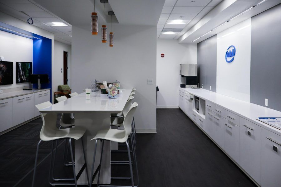 Modern office kitchen with white cabinets, island table, stools, and overhead pendant lights