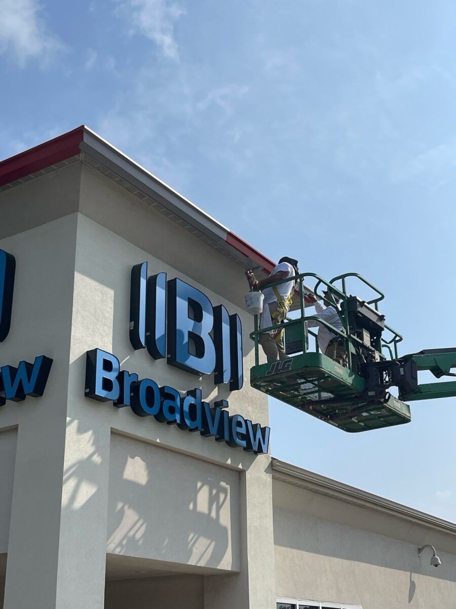 Worker in a green lift installing signage on a building exterior under a blue sky