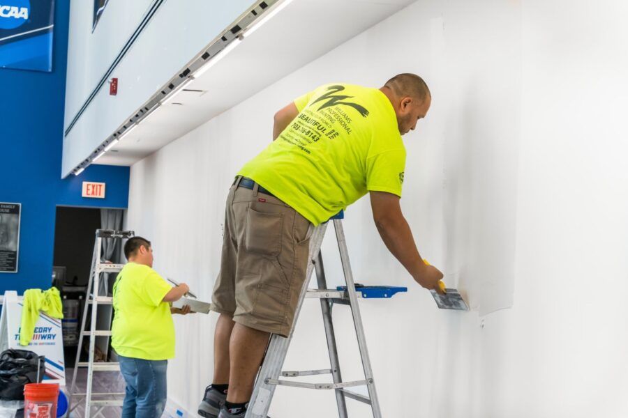 Workers painting a white wall on ladders inside a bright commercial building