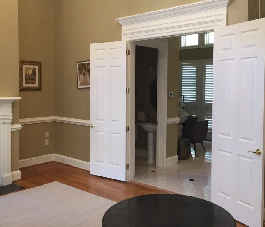 Open double doors to a bright tiled room from a tan living room with hardwood floors.