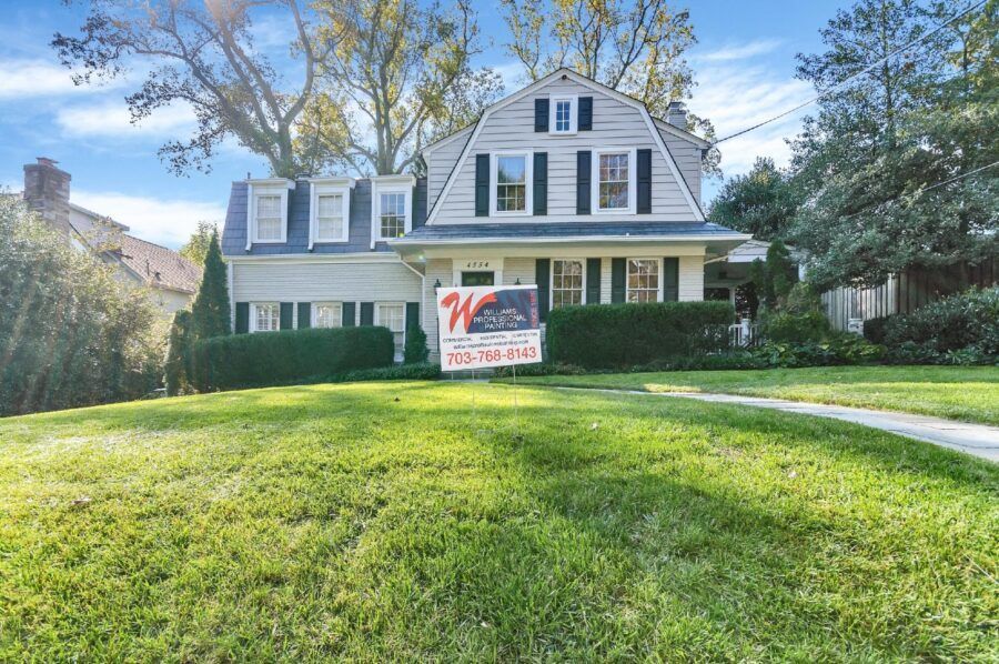 Two-story white house with green shutters and a lawn sign in the front yard on a sunny day